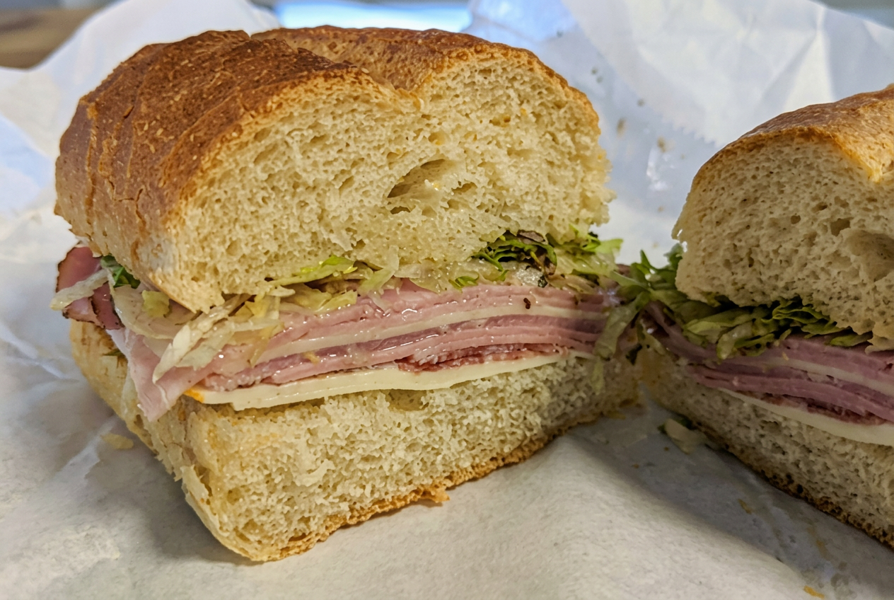 Hands stacking Italian cold cuts on a hard-crust roll